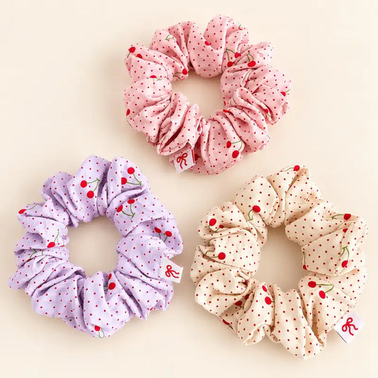 Cute cherry polka dot hair scrunchies in pastel pink, purple and cream with soft ruffled fabric.