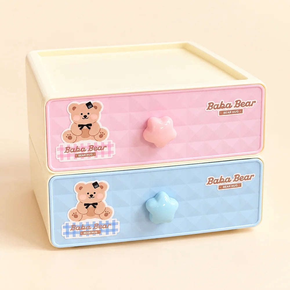 A stack of two cute plastic drawer organizers with cream-colored outer frames. The top drawer is pastel pink with a quilted pattern, a pink star-shaped knob, and a cartoon teddy bear sticker.