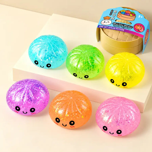 Colourful glitter bun squishy toys with cute kawaii faces, sparkly translucent finish, and mini steamer-style packaging.