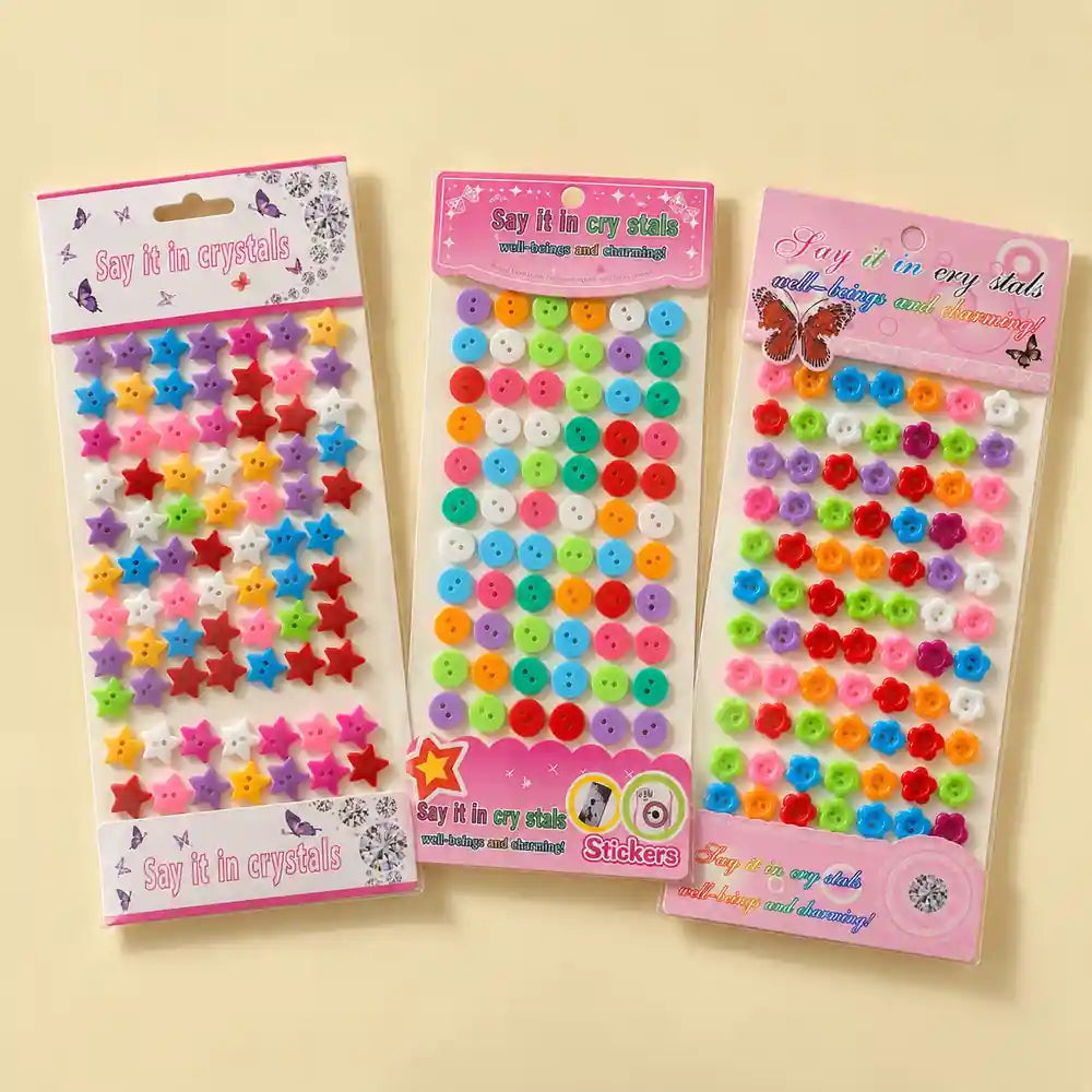 Three packages of colorful craft embellishments labeled 'Say it in cry stasis' on a light beige background. The left package contains pastel and bright star-shaped crystals, the middle contains round multicolor beads, and the right package contains round multicolor stickers.