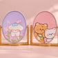 Kawaii oval tabletop mirrors with cute pastel character designs and wooden stands on a soft pink background.