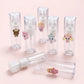 Several small clear plastic spray bottles with white pump caps are arranged on a pale pink background. Each bottle has a small colorful cartoon character attached near the top, and one bottle is shown uncapped with its cap placed beside it.