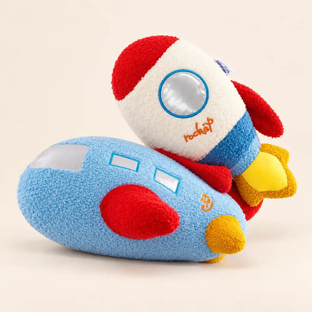 A plush toy set featuring a blue airplane and a red, white, and blue rocket ship with yellow flames, photographed on a solid light beige background.